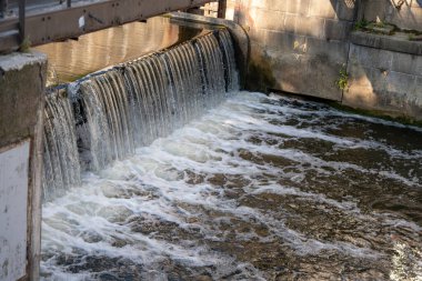 Küçük bir şelale bir hendeğin üzerinden nehre akıyor. Yapı endüstriyel yapı ve akan suyun kombinasyonunu gösteriyor..