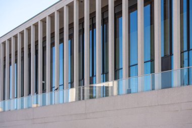 Dikey beton destekli ve sürekli cam cepheli modern bir bina. Temiz çizgiler ve yansımalar minimalist bir estetik yaratıyor..