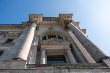 Sütunlu Neoklasik Cephe. Büyük taş sütunları ve süslemeleri olan neoklasik bir binanın yukarı bakış açısı. Açık mavi gökyüzü anıtsal yapıyı çerçeveler..