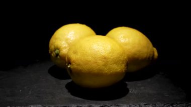 Siyah arka planda üç limon. Üç parlak limon koyu bir arka planda dönüyor. Sarı kabuk öne çıkar ve taze ve keskin görünür..