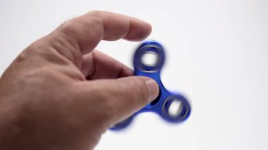 Metalik, mavi, el ele tutuşup dönen bir fırıldak. Döndürücü hızlı döner, beyaz arkaplan üzerinde bulanık bir etki yaratır.