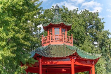 Çin Pavyonu. Geleneksel kırmızı ve yeşil bir Çin pavyonu mavi bir gökyüzünün altında yemyeşil ağaçlarla çevrilidir. Süslü çatısı ve karmaşık mimarisi güneş ışığını çok güzel yakalıyor..