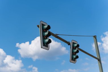 Mavi gökyüzüne karşı trafik ışıkları. Bulutlu bir gökyüzüne karşı iki trafik lambası, aşağıdan hafifçe fotoğraflanmış. Trafik ve şehir hayatı için sembolik fotoğraf.