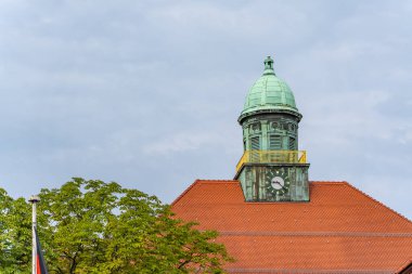 Saat ve Kırmızı Çatı 'lı Bakır Kule. Ağaçların üzerinde yeşil bakır kubbesi ve kırmızı kiremitli çatısı olan tarihi bir saat kulesi. Saat 10 'u gösteriyor ve gökyüzü bulutlu..