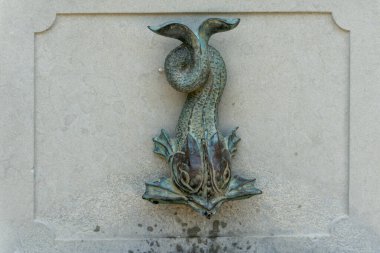Bronz Dolphin Çeşmesi. Dekoratif bronz yunus şeklindeki bir çıkıntı taştan bir duvara monte edilmiştir..