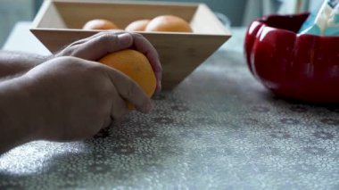 Peel Orange 'a başlıyoruz. Eller taze bir portakalın kabuğuna bastırarak deriyi yüzmeye başlıyor. Arka planda bir kase portakal var..