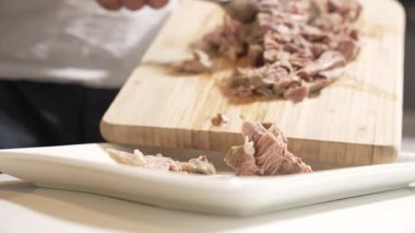 Dilimlenmiş et servisi. Bir el, yumuşak, kaynamış eti kesme tahtasından beyaz bir tabağa aktarmak için çatal kullanır. Sulu dokusu açıkça görülüyor..