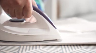 Buhar ütüsü desenli bir tahtanın üzerine beyaz bir giysi ütüler. Eller kumaşı mükemmel bir bitiş için ayarlar..