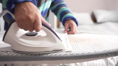 Kişi desenli bir tahta üzerinde beyaz bir gömlek ütülüyor, kumaşı sabit tutuyor. Buhar pürüzsüzleştirir kırışıklıkları Çıtır çıtır bir görünüş için.