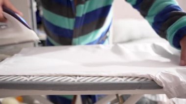 Buharlı ütüyü yakın plan beyaz gömlek ütülüyor. Desenli ütü masası düz kumaşla çelişiyor..