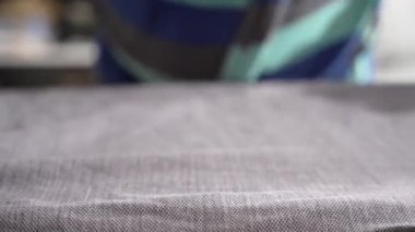 Gri dokuma demiri düzleştiren bir kumaşın yakın çekimi. Buhar yavaşça yükseliyor kırışıklıklar kaybolurken.