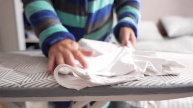 Beyaz bir tişört desenli ütü masasının üzerinde duruyor, basılmaya hazır. Eller ütülemeden önce kumaşı ayarlar.