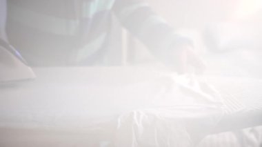 Beyaz bir gömlek bir tahtaya ütülendiğinde buhar yükselir. Yumuşak ışık pürüzsüz kumaş yüzeyini vurgular.