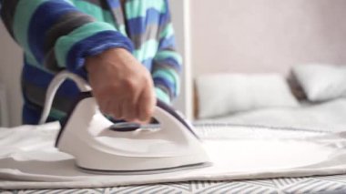 Çizgili bornozlu bir insan desenli bir tahtada beyaz bir kumaşı ütüler. Ütü elbisenin üzerinde pürüzsüzce süzülür..