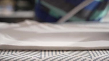 Bir buhar ütüsü desenli ütü masasında beyaz bir gömleğin üzerinden süzülür. Pürüzsüz, pürüzsüz sona odaklanıyoruz..