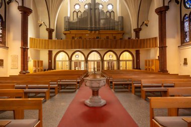 Büyük organı ve ahşap bankları doğrudan gören bir körfez. Vaftiz fontu ön planda..