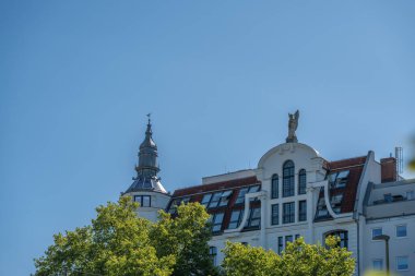 Ağaçların tepesinde bir kulesi ve heykeli olan bir Berlin binasının yakın çekimi. Arka planda mavi gökyüzü.