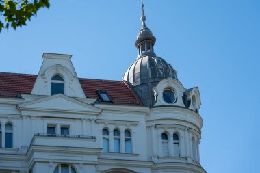 Kubbesi ve süslü pencereleri olan zarif, eski bir bina çatısı. Parlak mavi gökyüzüne karşı tarihi mimari.