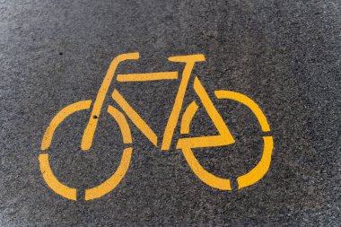 Asfalta sarı bir bisiklet sembolü çizilmiş, bisiklet yolunu işaret ediyor. Gri yüzeyde belirgin bir işaret var..