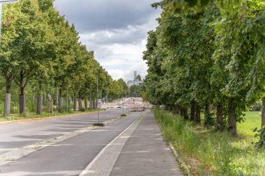 Yeşil ağaçlarla kaplı sessiz bir yol bloklanmış bir inşaat alanına çıkıyor. Yol boş ve sakin..