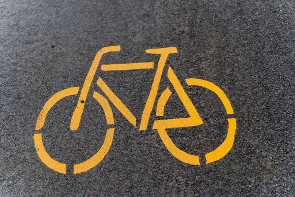 Asfalta sarı bir bisiklet sembolü çizilmiş, bisiklet yolunu işaret ediyor. Gri yüzeyde belirgin bir işaret var..