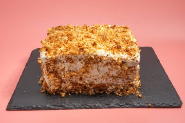 Krem şantili dikdörtgen pasta ve siyah tabakta kırıntı süsü. Pembe arkaplan.