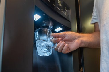 Bir bardak modern bir su dağıtıcısından suyla dolduruluyor. İşlem sırasında bir el bardağı tutar..