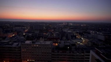 Bir panoramik kamera taraması alacakaranlıkta parlayan ışıkları ve ufukta kaybolan bir günbatımını yakalar. Gündüzden geceye geçiş gökyüzü ve atmosferi vurguluyor..