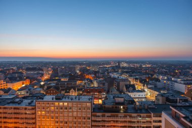 Karanlık çöktüğünde kasaba ışıkları parlıyor, günbatımı ufukta kayboluyor. Sokaklar ve binalar alacakaranlık gökyüzünün altında aydınlanıyor.