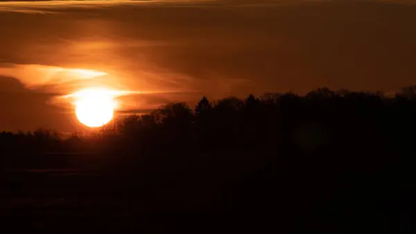 Ormanın üzerinde güzel, vahşi bir gün doğumu. Turuncu bulutlu gökyüzü. Bulutların arkasındaki güneş