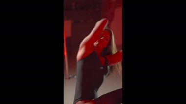 Uzun saçlı, zayıf, esmer bir kadın kulüpte kırmızı ışıklarla dans ediyor. Dikey 4K görüntü.