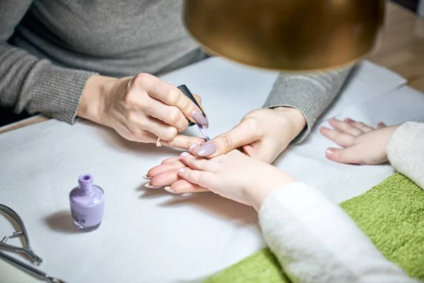 Closeup of a happy beautician doing manicure to a small girl under the gold lamp in the nail salon. Child getting a nail manicure.