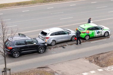 Riga, Letonya - 15 Şubat 2023: bir şehir caddesinde üç araba kazası. Bir sürücü kaza yapmış arabaların yanında duruyor ve sigorta için belgeleri dolduruyor..