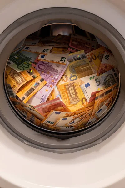 Closeup of a big pile of money in an open washing machine. Money laundering concept. Vertical shot.