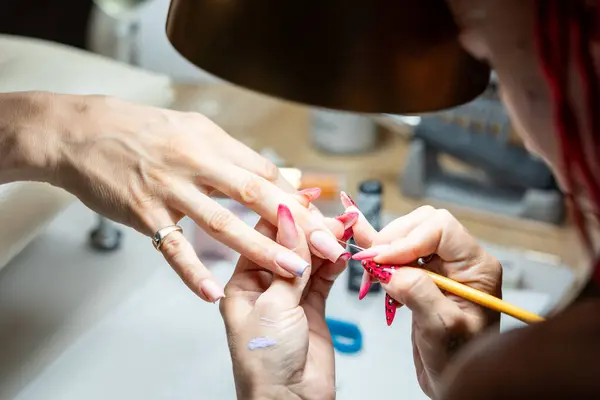 Close-up shot of a woman hand in a nail salon receiving manicure by beautician with brush. Woman getting nail manicure at spa centre.