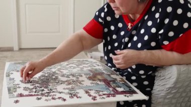 Son sınıf öğrencisi bir kadın evdeki rahat parlak odasında sandalyesinde otururken yapboz topluyor. 4k görüntü