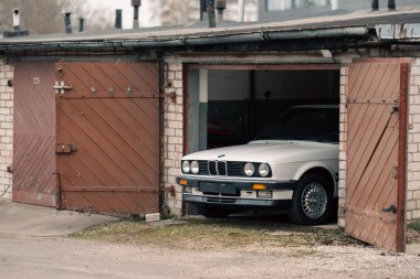 Riga, Letonya - 1 Nisan 2024: Açılmış garajdaki beyaz klasik BMW E30 arabası.
