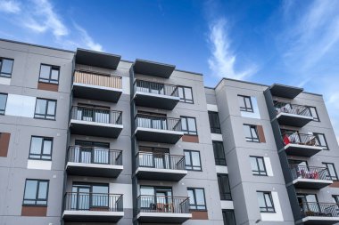Göz kamaştırıcı mavi bir arkaplan karşısında geniş balkonlar gösteren modern ve şık bir apartman kompleksi.