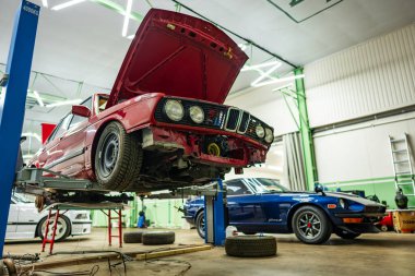 Tam donanımlı bir otomotiv atölyesinde, iki klasik araba dikkatle bakılıyor.