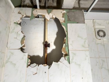 Tesisat tesisatı ve kırık fayanslarda paslı görünür bir borunun içinde, önemli ölçüde hasar görmüş bir duvarın detaylı bir yakın çekim görüntüsü.