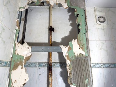 Tesisat tesisatı ve kırık fayanslarda paslı görünür bir borunun içinde, önemli ölçüde hasar görmüş bir duvarın detaylı bir yakın çekim görüntüsü.