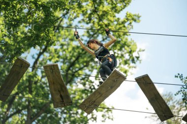 Kararlı bir kadın, doğanın güzelliğinde belirlenmiş zorlu yüksek ip engelli parkurunu başarıyla fetheder.