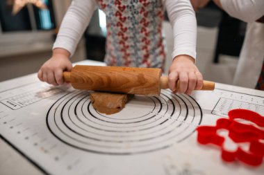 Bir çocuk yumuşak hamuru ahşap bir broşla atıyor, sıcak, neşeli bir tatil mutfağında şenlikli kurabiyeler yapıyor.