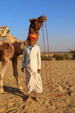 THAR RAJASTHAN INDIA - 02 13 2023: Thar çölünün kum tepelerinde develeri olan Hint deve sürücüsü. Jaisalmer, Rajasthan, Hindistan