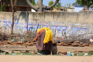 RURAL RAJASTHAN INDIA - 02: 15 2023: evsiz kadın yol kenarındaki çöpte bir şeyler bulmaya çalışıyor