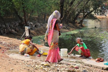 KHAJURAHO INDIA MADYHA PRADESH - 03 2023: Kadınlar elbiselerini yıkıyor. Hindistan 'daki fakir insanlar elbiselerini bir nehrin kıyısında yıkayıp kurutuyorlar.