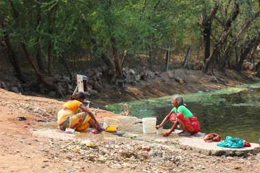 KHAJURAHO INDIA MADYHA PRADESH - 03 2023: Kadınlar elbiselerini yıkıyor. Hindistan 'daki fakir insanlar elbiselerini bir nehrin kıyısında yıkayıp kurutuyorlar.