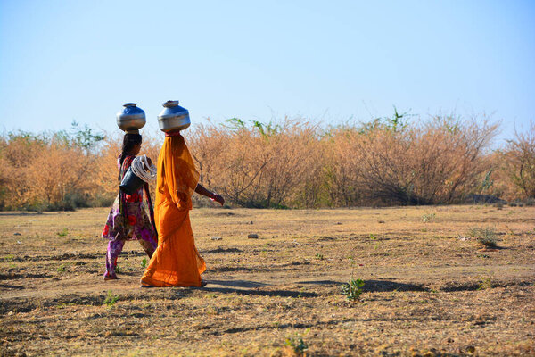 THAR DESERT JAISALMER RAJASTHAN INDIA - 02 13 2023: Rajasthani women carrying water jars in the head. The country has 18 percent of the world's population, but only 4 percent of its water resources 