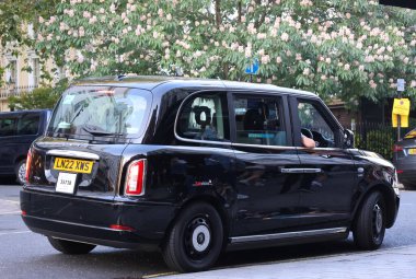 LONDRA BİRLİK KINGDOM 06 19 2023: Tipik siyah Londra taksisi şehir sokaklarında. Geleneksel olarak taksi Londra 'da siyahtır ama şimdi farklı renklerde üretiliyor..