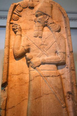 LONDRA BİRLİK KINGDOM 06 17 2023: Ashurnasirpal II kireçtaşı stela: oyulmuş; kral kraliyet şapkasını konik bir üst ile giyer ve otoriteyi sembolize eden bir gürz tutar